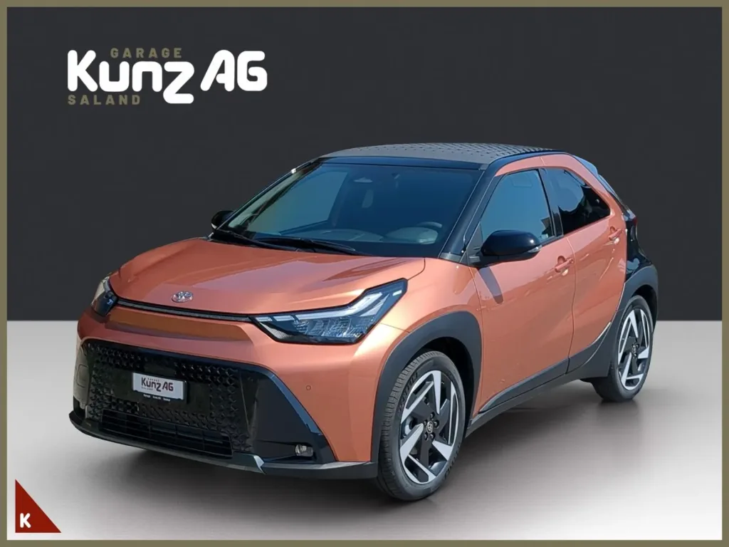Schräge Frontansicht eines kupferfarbenen Toyota Aygo X Style mit schwarzem Dach vor grauem Hintergrund.