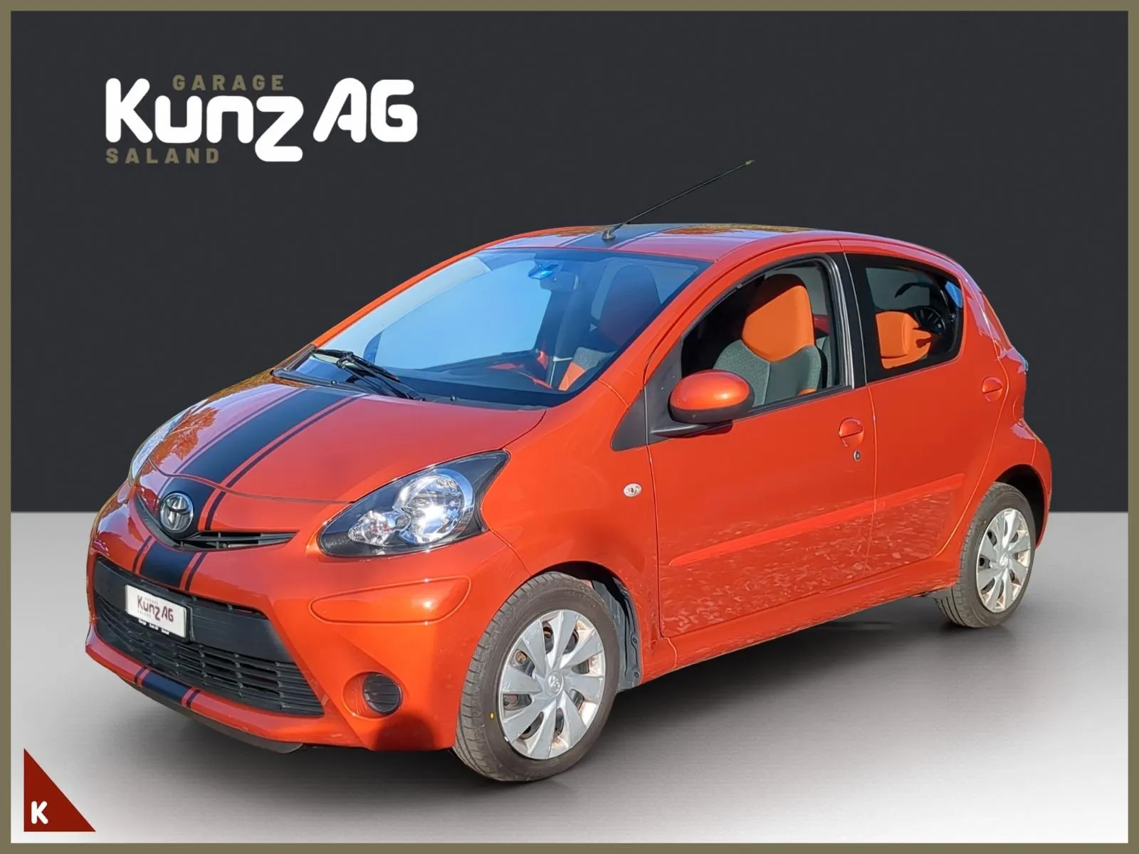 Schrägansicht von vorne links auf einen orangefarbenen Toyota 1.0 VVT-i Linea Luna Spicy vor grauem Hintergrund