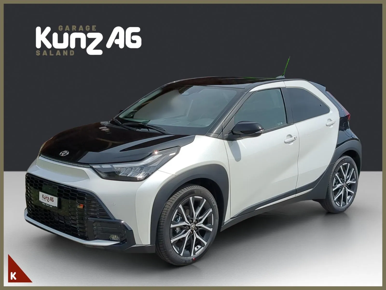 Schrägansicht von vorne links eines weiss-schwarzen Toyota Aygo X GR Sport vor grauem Hintergrund.
